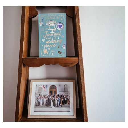 Roman Journal d’une wedding planner de Sophie Jomain posé sur une étagère en bois au-dessus d’une photo de mariage encadrée
