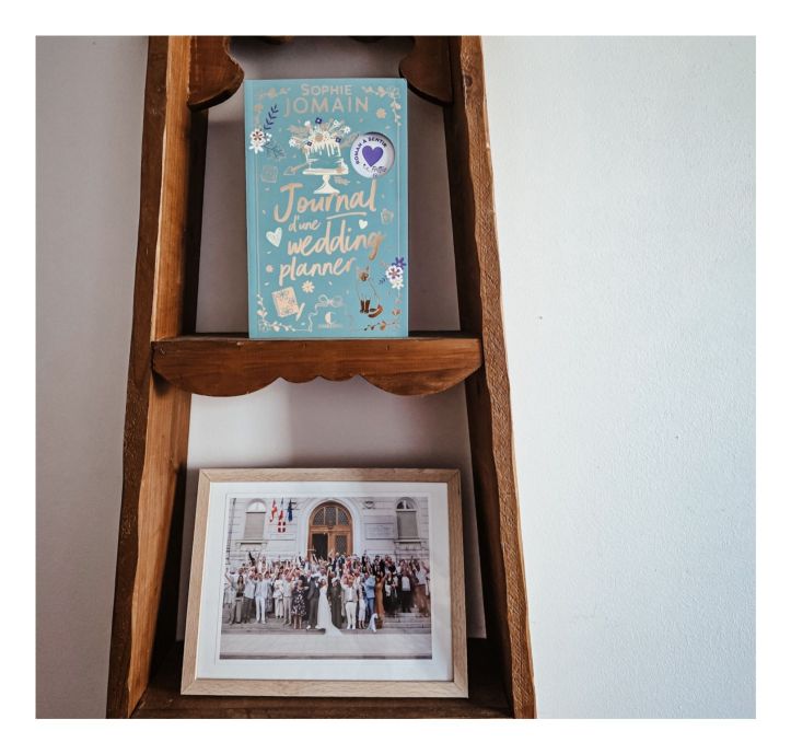 Roman Journal d’une wedding planner de Sophie Jomain posé sur une étagère en bois au-dessus d’une photo de mariage encadrée