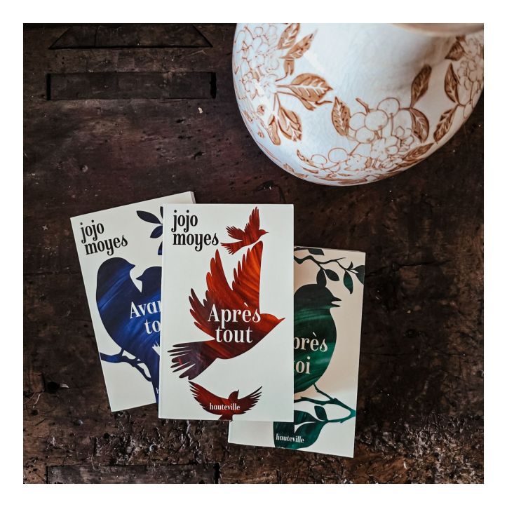 Romans de Jojo Moyes posés sur une table en bois à côté d’un vase fleuri